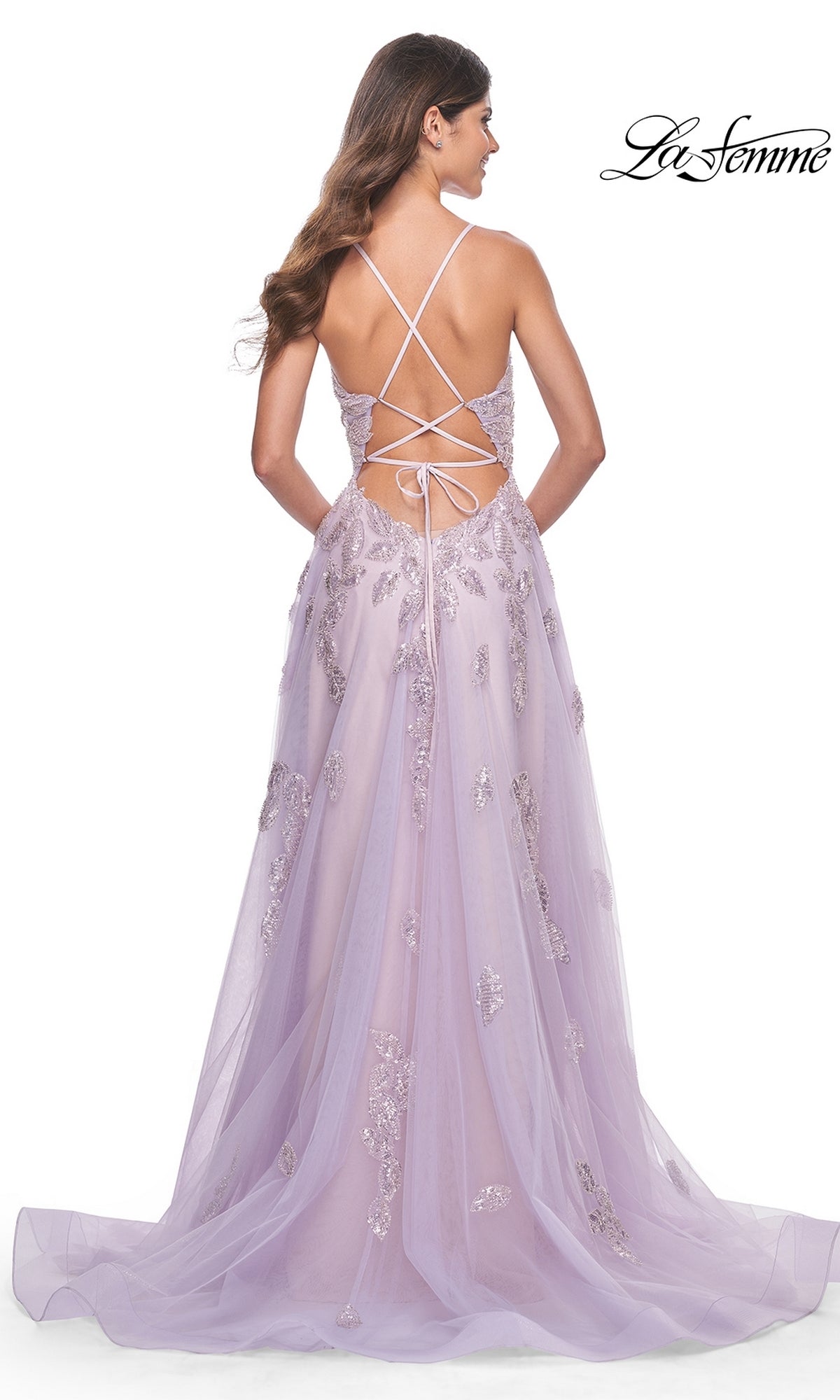 Woman in the La Femme Sequin-Embroidered Long Prom Dress 32090, a lavender A-line gown with flowing tulle, sequin embroidery, sparkling accents, and a lace-up open back, stands facing away.